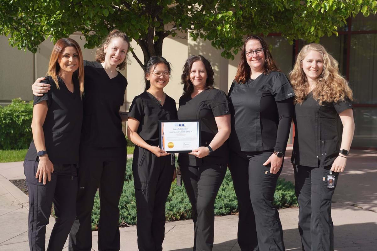 Six women standing next to each other wearing black scrubs holding on to a certificate and smiling