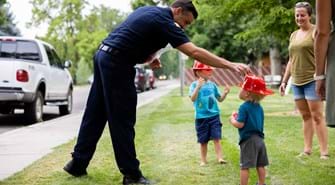firefighter helping young boy with his red fire fighter hat