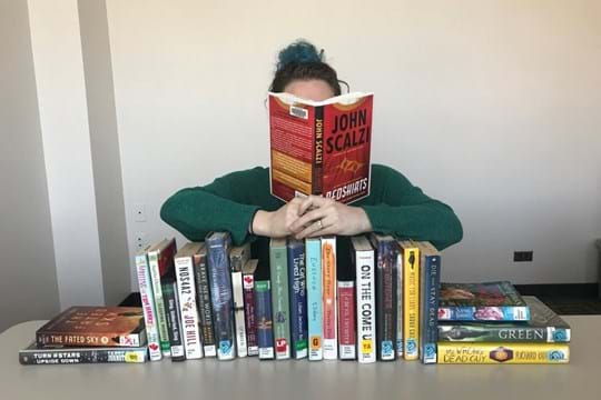 Person reading a book with a stack of books in front of them.