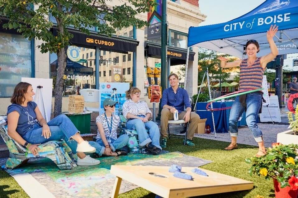 City of Boise repurposes parking space into social space with tent, people sitting in chairs, and outdoor game.