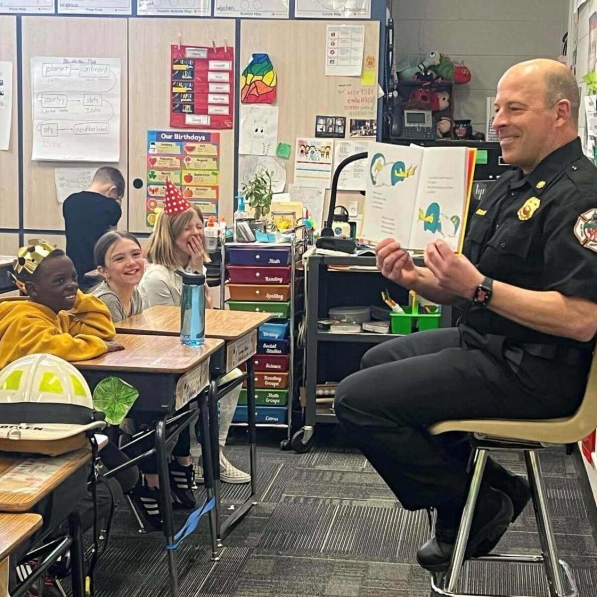 Firefighter in a classroom reading a book to a group of kids.