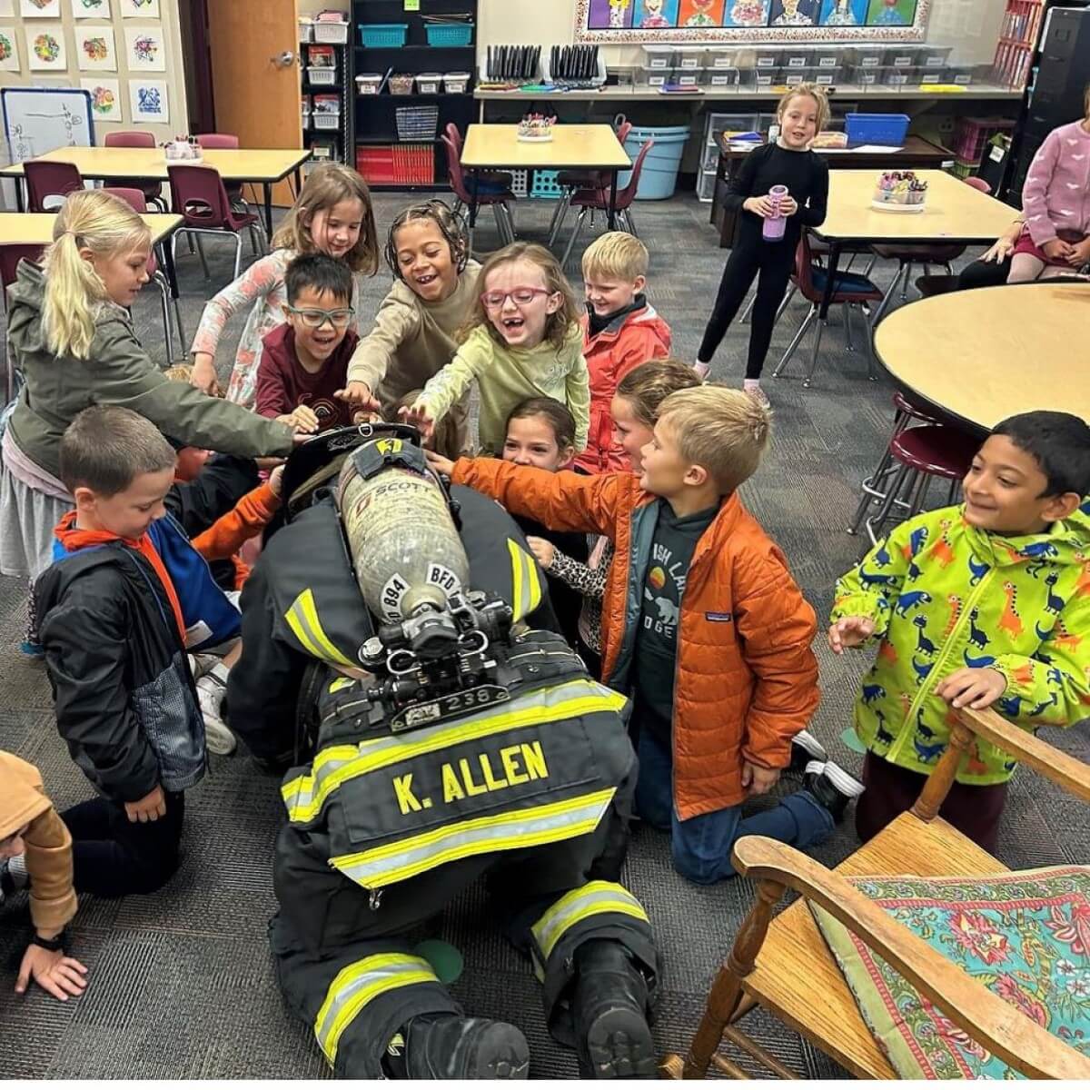 Firefighter kneeling down with small children feeling his helmet. 