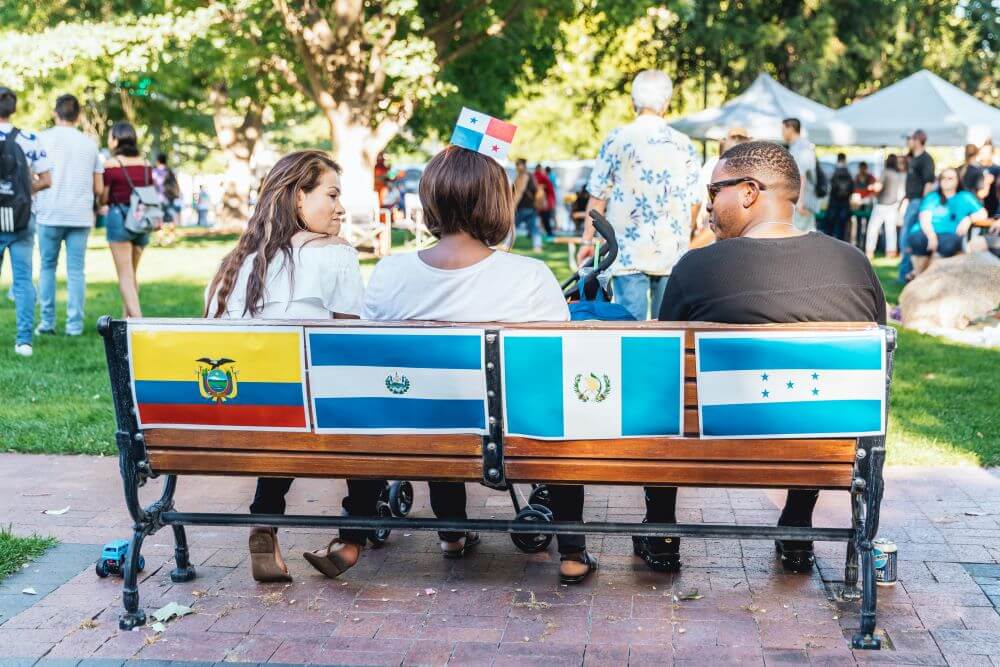 People sitting at a park bench with flags of various countries behind them.
