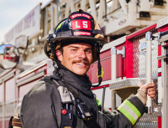 A firefighter holds on to a fire truck outside.