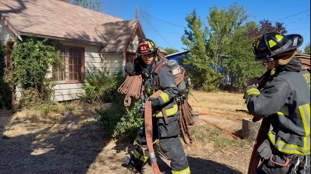 Two firefighters use a hose in front of a house.