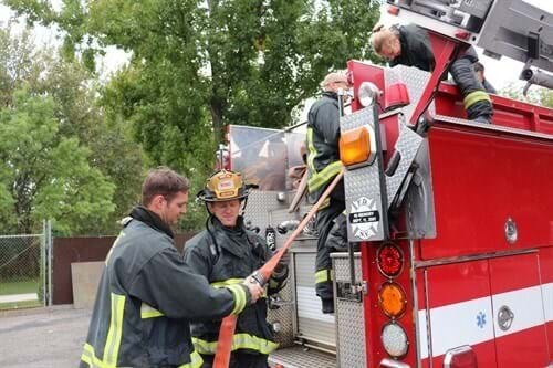 Two firefighters adjust a hose on the back of a fire engine.