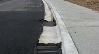 Photo of street with drains next to curb and sidewalk with drop inlets in drains