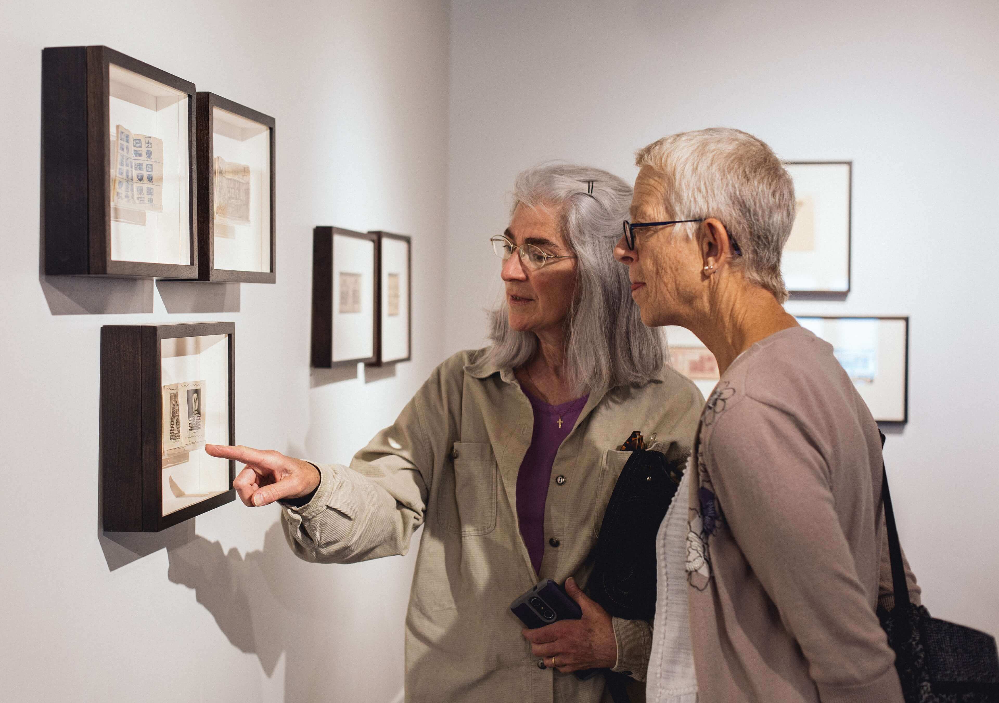 Two women look at sketches hanging on a wall.