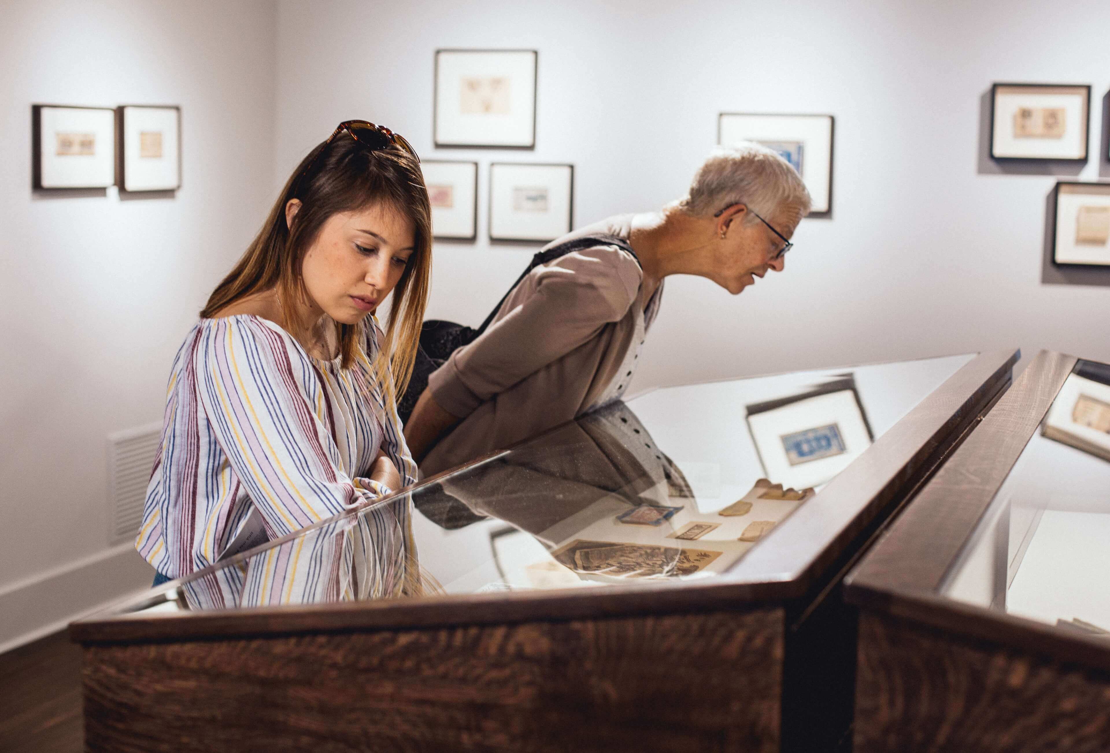 Two women look at art display in a glass covered display case.