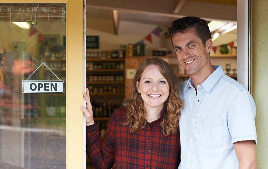 Couple standing in front of their business with an open sign