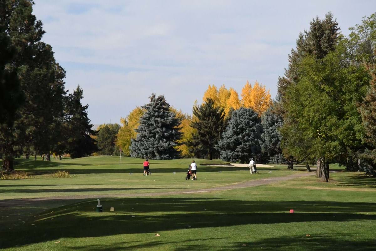 Warm Springs Golf Course with green grass and yellow, green and blue changing trees throughout. Three golfers on the golfing greens.