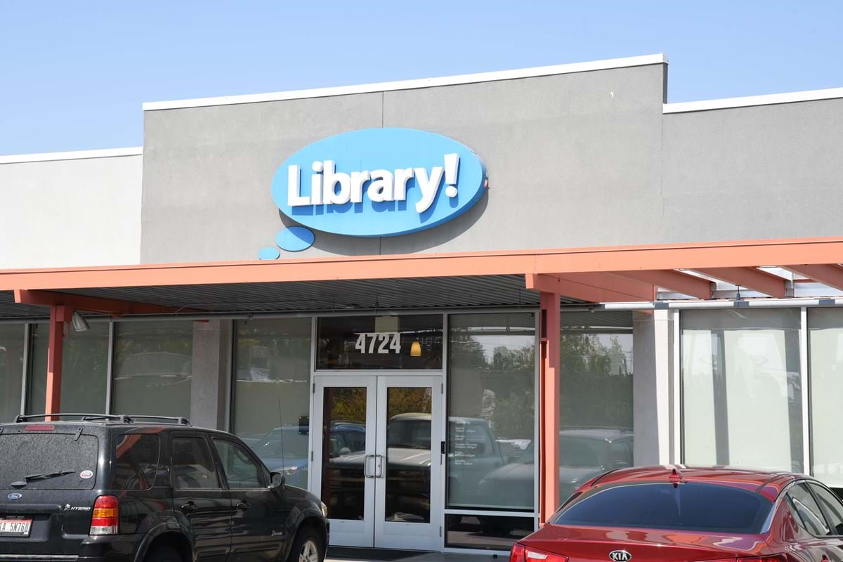 Library! sign above pergola covering front door with black and red car in parking lot in front of building