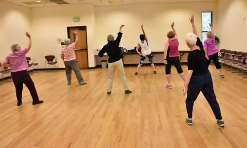 Group of senior women taking a Zumba class. Their arms are stretched over their heads.
