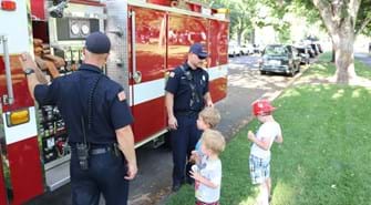 Firefighters standing in front of firetruck with kids