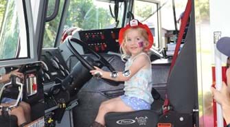 Small child in drivers seat of fire truck with fire fighter