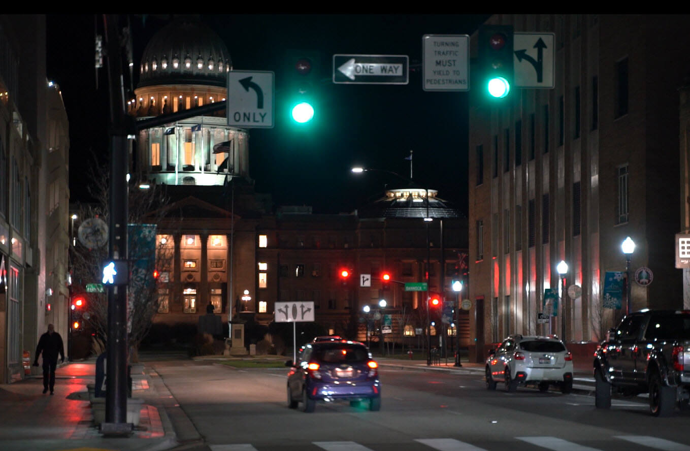 Nighttime downtown street with cars and green lights to proceed.